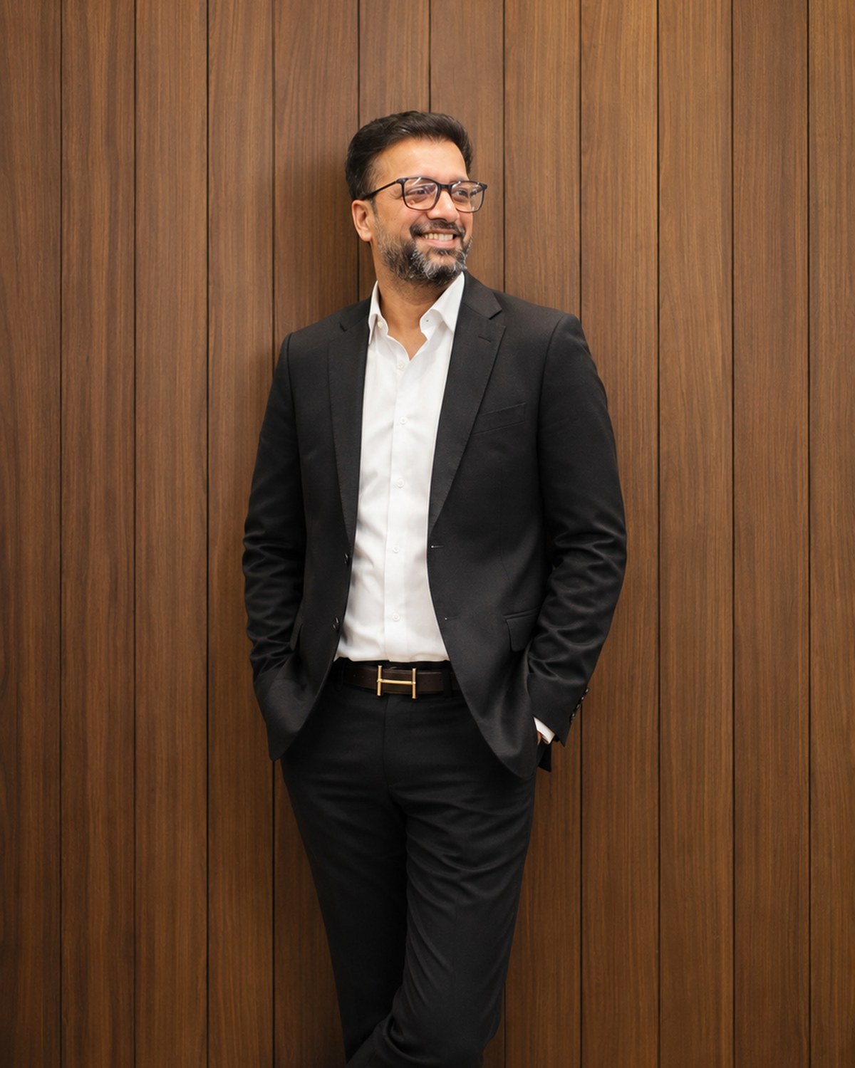 Sahil Jindal in a black suit smiling against a walnut panelled wall