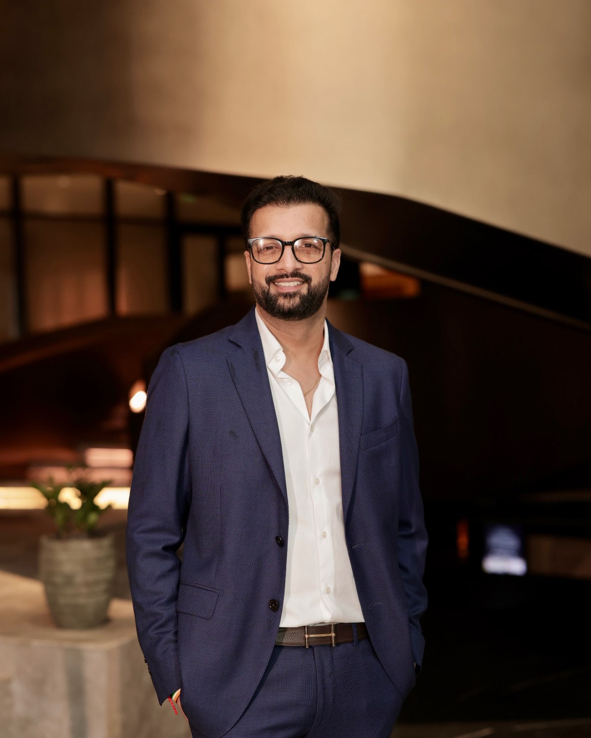Sahil Jindal in a navy suit in front of a curved architectural staircase