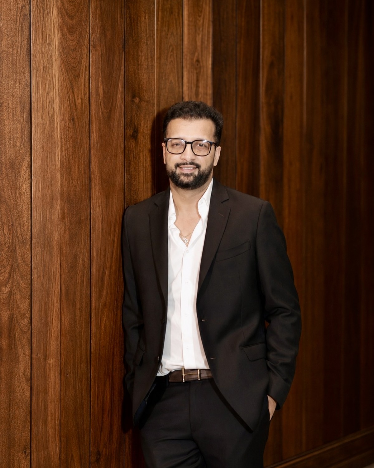 Portrait of Sahil Jindal in a black suit against a walnut panelled wall