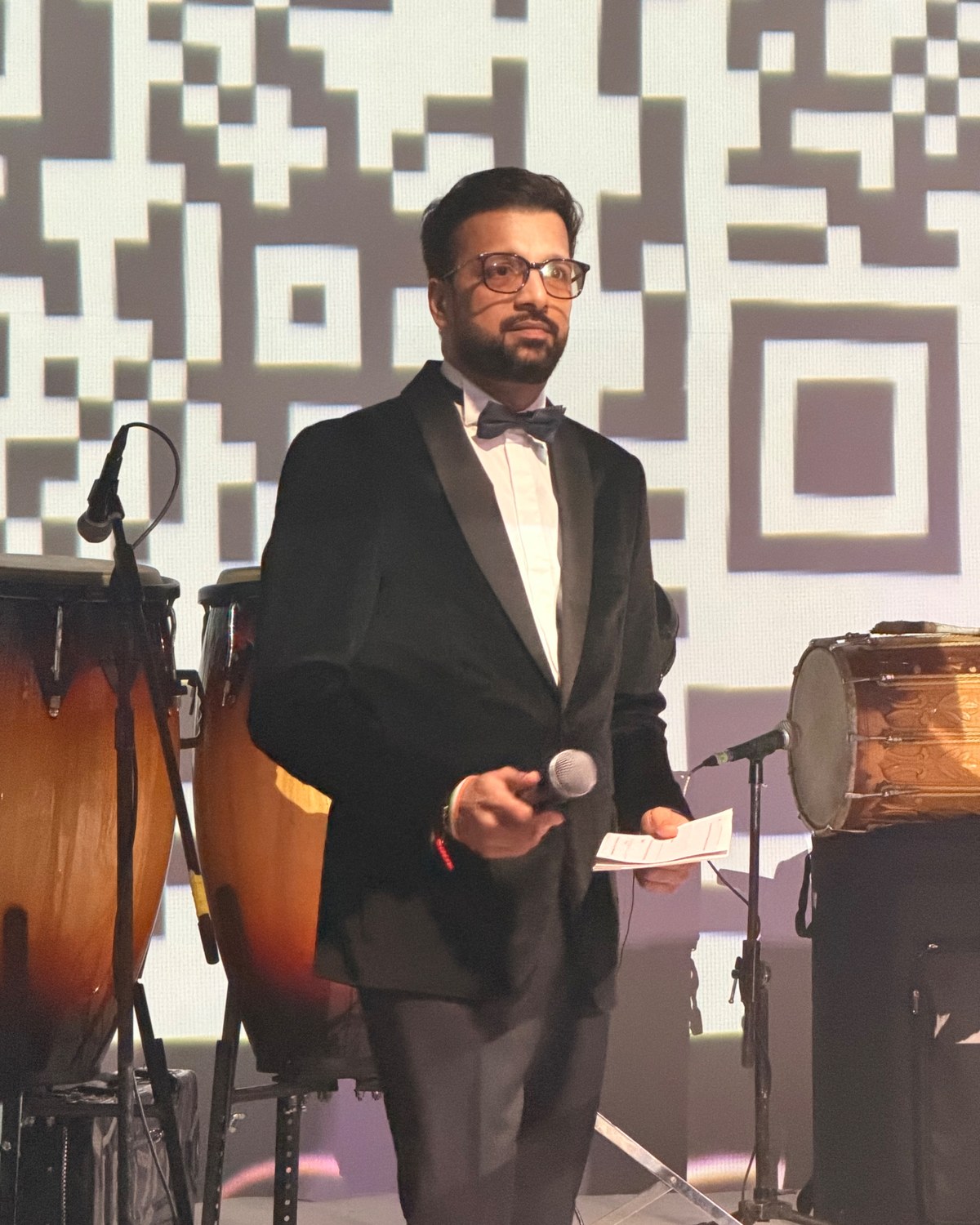 Sahil Jindal in black tie holding a microphone on stage at an awards evening